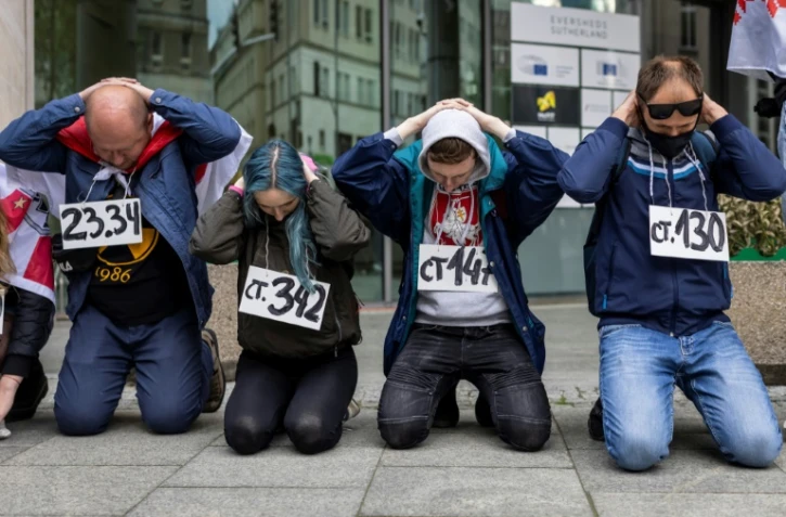 Des militants bélarusses manifestent devant les bureaux de la Commission européenne à Varsovie le 29 mai 2021 en posant comme s'ils étaient arrêtés, avec sur la poitrine la référence d'un article du code pénal invoqué pour l'arrestation du journaliste dissident Roman Protassevitch
