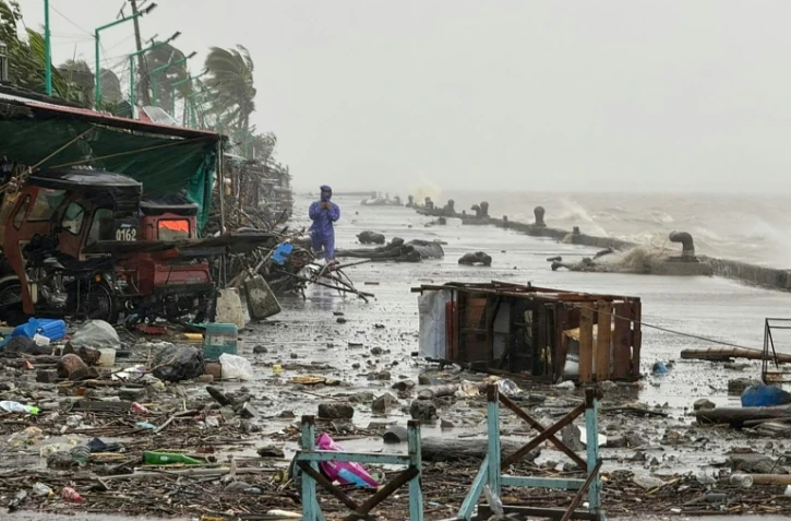 Un homme se tient à côté de débris près du bord de mer, le 22 septembre 2025 à Aparri aux Philippines