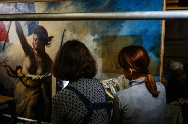 Des restaurateurs travaillent sur le tableau "La liberté guidant le peuple" d'Eugène Delacroix, dans un laboratoire du Musée du Louvre à Paris, le 28 février 2024