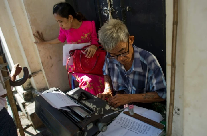 Aung Min, un des rares écrivains publics restant dans la capitale birmane Rangoun, travaille sur le document d'une cliente dans la rue Pansodan, le 5 décembre 2018