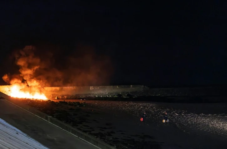 Des policiers éloignent des bidons d'essence d'un canot en feu sur la plage du Portel (Pas-de-Calais) le 21 septembre 2024