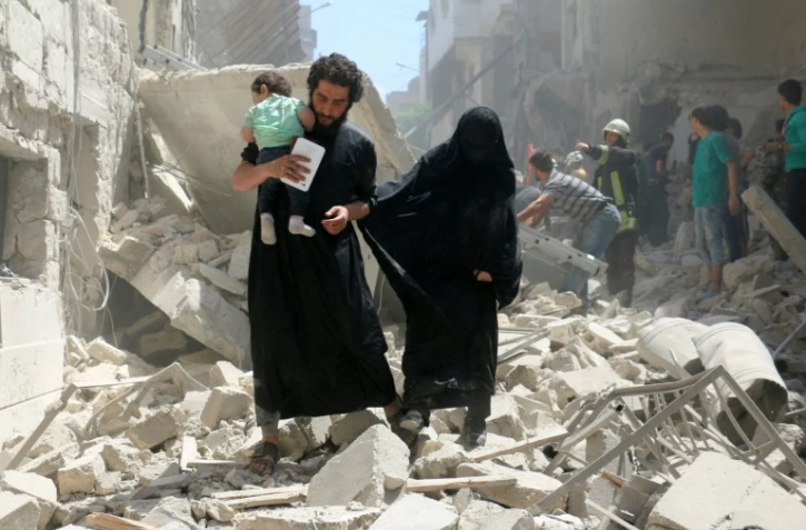 Une famille parmi les décombres d'habitations bombardées dans une zone détenue par les rebelles à Alep, le 28 avril 2016