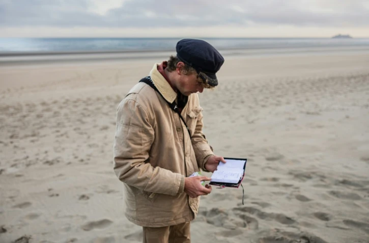 Le "beachcomber" belge Aäron Fabrice de Kisangani regarde un carnet abandonné par des migrants sur la plage de Gravelines, le 26 mars 2025 dans le Nord