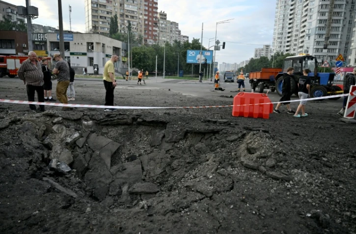 Des habitants de Kiev passent près d'un cratère causé par une frappe de missile russe sur la capitale de l'Ukraine, le 11 juillet 2026