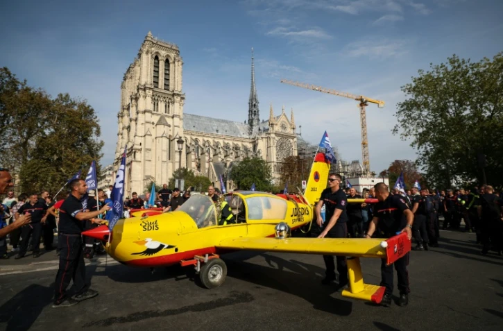 Des pompiers installent un avion peint aux couleurs de la Sécurité civile devant la cathédrale Notre-Dame de Paris, lors d'une manifestation pour réclamer des hausses de salaires et des moyens budgétaires accrus, le 28 septembre 2026 à Paris