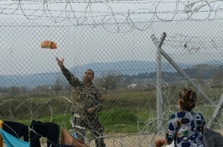 Un soldat macédonien lance du pain à une réfugiée, à la frontière entre la Macédoine et la Grèce, dans le camp de fortune d'Idomeni en Grèce, le 1er avril 2016