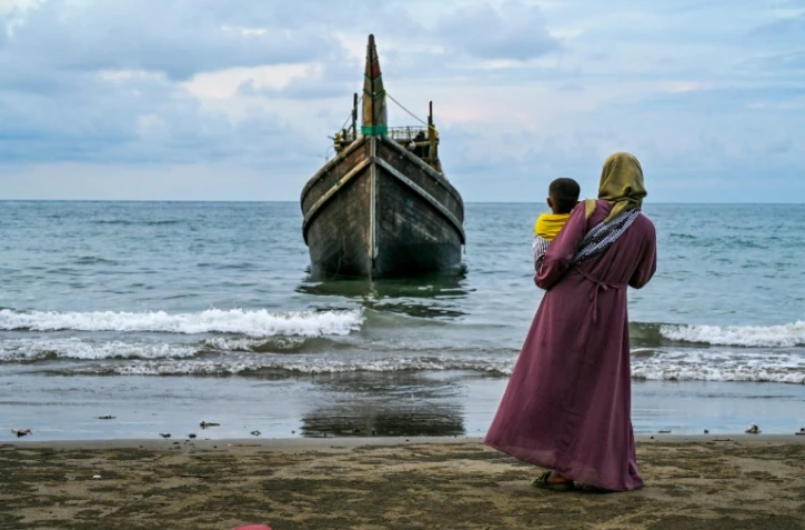 Une femme et son enfant devant l'embarcation qui a transporté des centaines de réfugiés Rohingyas jusqu'à la
plage de Laweueng, en Indonésie, où ils ont accosté après avoir fui les camps du Bangladesh, le 10 décembre 2023