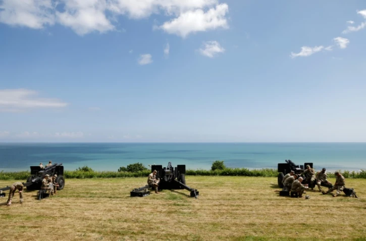 Des militaires américains se rassemblent près de canons d'artillerie de campagne surplombant la plage d'Omaha et la Manche, près du cimetière américain de Colleville-sur-Mer, dans le nord-ouest de la France, le 5 juin 2024