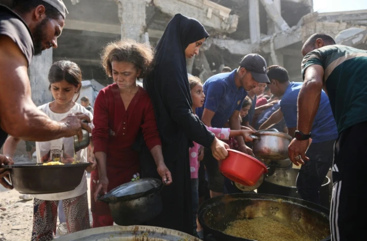Des Palestiniens déplacés attendent de recevoir de la nourriture à l'extérieur de la mosquée Imam al Shafi'i en ruines, où des familles ont trouvé refuge, dans le quartier de Zeitoun à Gaza, le 23 octobre 2025