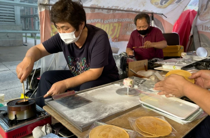 Jung Jung-soon (G) et son mari Lim Chang-joo confectionnent leurs "dalgonas", friandise rendue célèbre par la série Squid Game, à Séoul le 10 octobre 2021