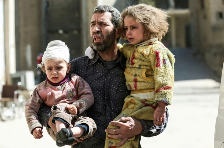 Un Syrien tient dans ses bras deux enfants blessés après une frappe aérienne à Hamouria près de Damas qui a fait au moins 16 civils morts et des dizaines de blessés le 25 mars 2017