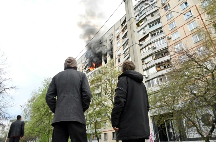 Des passants observent l'incendie provoqué par une frappe dans un appartement des faubourgs nord de Kharkiv, dans l'est de l'Ukraine, le 22 avril 2022