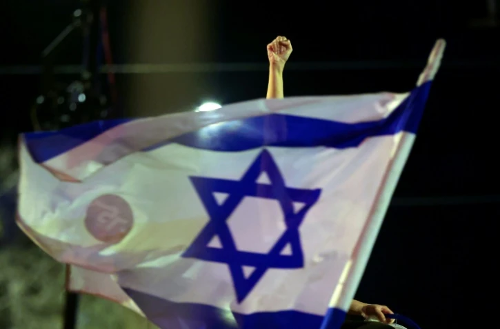 Un manifestant lève le poing derrière un drapeau israélien lors d'une manifestation anti-gouvernementale près de la résidence du Premier ministre israélien à Jérusalem, le 20 mars 2021, avant les législatives du 23