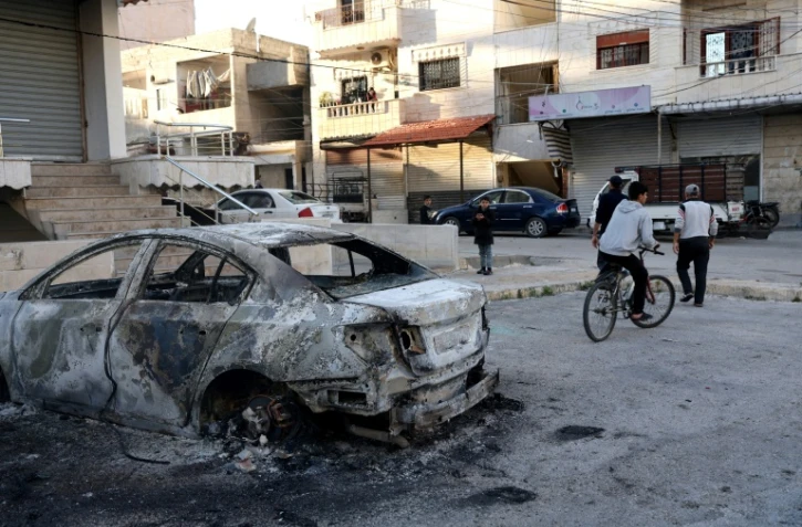 Un jeune fait du vélo à côté d'une voiture détruite après les affrontements entre les nouvelles autorités syriennes et les partisans du président déchu Bachar al-Assad dans la ville de Jableh, dans la province côtière de Lattaquié, le 10 mars 2025