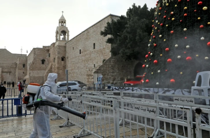Un employé en combinaison de protection désinfecte les abords de l'église de la Nativité, avant les célébrations de Noël, le 24 décembre 2020 à Bethléem
