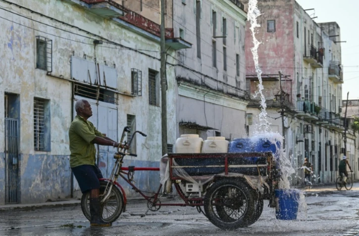 Un homme remplit des récipients d'eau à un point de ravitaillement public dans une rue de La Havane, le 5 octobre 2026