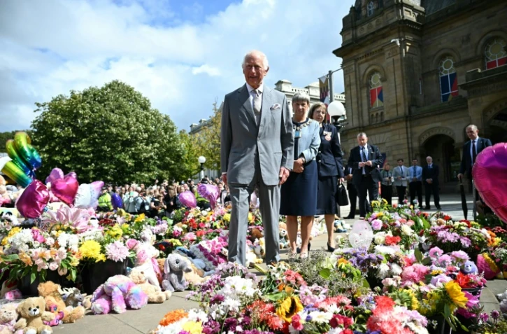 Le roi Charles IIIl s'arrête devant les fleurs déposées devant la mairie, après le meurtre de trois fillettes fin juillet dans une attaque au couteau, lors de sa visite pour rencontrer les membres de la communauté locale, le 20 août 2024 à Southport, au nord-ouest de l'Angleterre