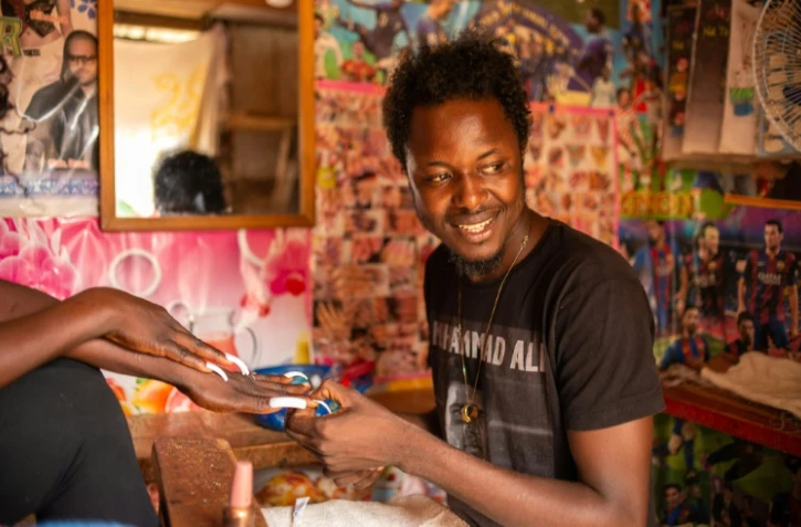 Debonheur Koli dans son échoppe avec une cliente venue pour une manucure, à Bangui le 14 juillet 2021  