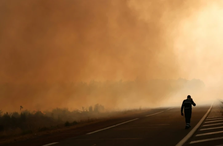 Un pompier marche sur une route à la lisière d'une zone en feu à Ares, le 26 juillet 2026, alors qu'un incendie de forêt ravage la forêt au nord du bassin d'Arcachon (Gironde) depuis le 22 juillet