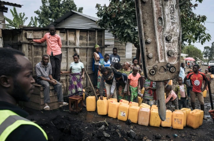Des habitants de Goma remplissent des bidons d'eau, le 28 mai 2021, pendant que des ouvriers réparent les canalisations rompues par l'éruption du volcan Nyiragongo, en RDCongo