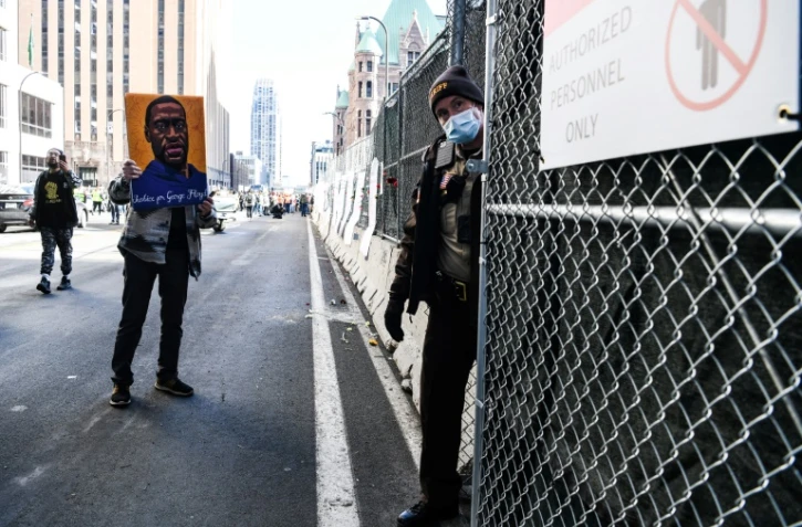 Un manifestant brandit une image de George Floyd devant un membre des forces de l'ordre, le 8 mars 2021, avant le début du procès de Derek Chauvin à Minneapolis