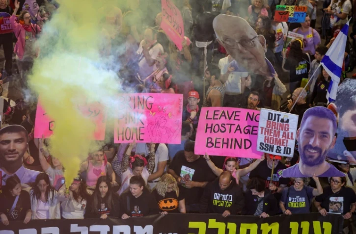 Des manifestants brandissent des pancartes et lancent des fusées éclairantes lors d'une manifestation appelant à la libération des otages encore retenus dans la bande de Gaza, à Tel-Aviv, le 15 mars 2025