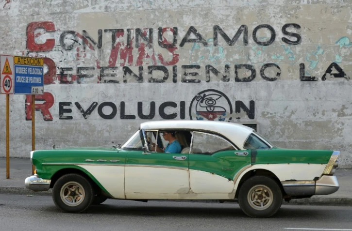 Une voiture passe devant un mur sur lequel s'affiche le slogan "Nous continuons à défendre la Révolution" en référence aux CDR, les Comités de défense de la révolution, le 20 mars 2018 à La Havane, à Cuba