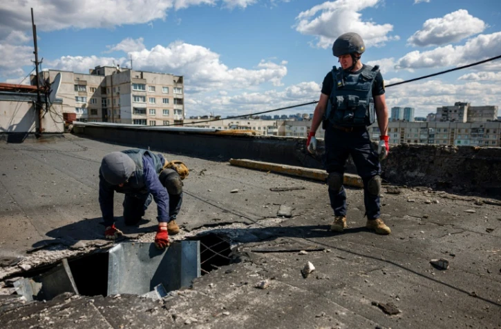 des membres d'une équipe de déminage examinent un engin explosif sur le toit d'un immeuble à Kharkiv, est de l'Ukraine, le 28 avril 2022
