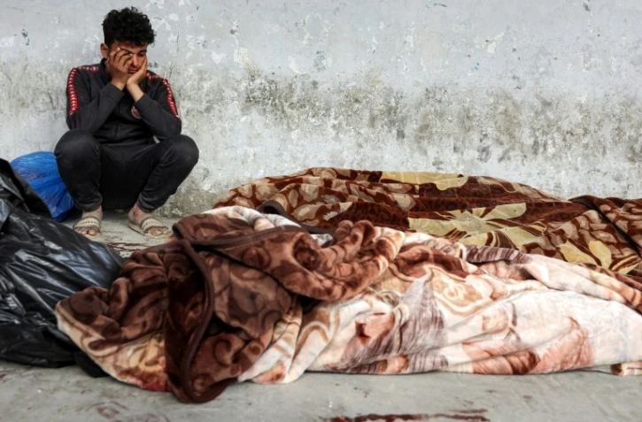 Un Palestinien pleure près de corps de proches tués dans un bombardement israélien à Gaza-ville et couverts de draps à l'hôpital Al-Ahli, le 18 mars 2025