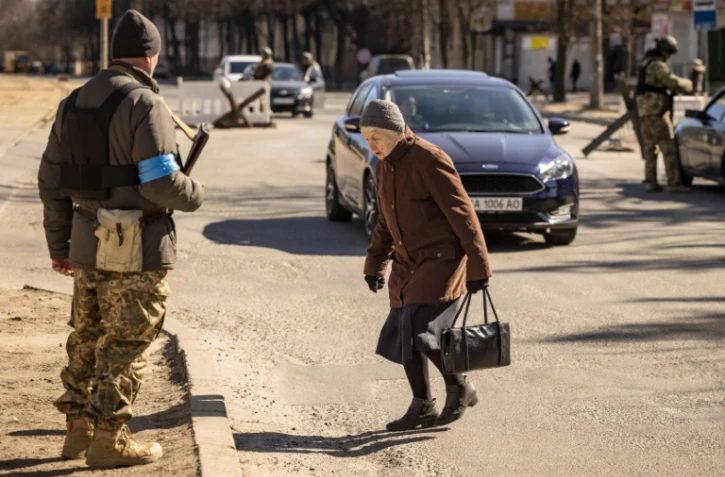 Une femme traverse une chaussée devant des membres des forces ukrainiennes à un point de contrôle à Kiev, le 21 mars 2022
