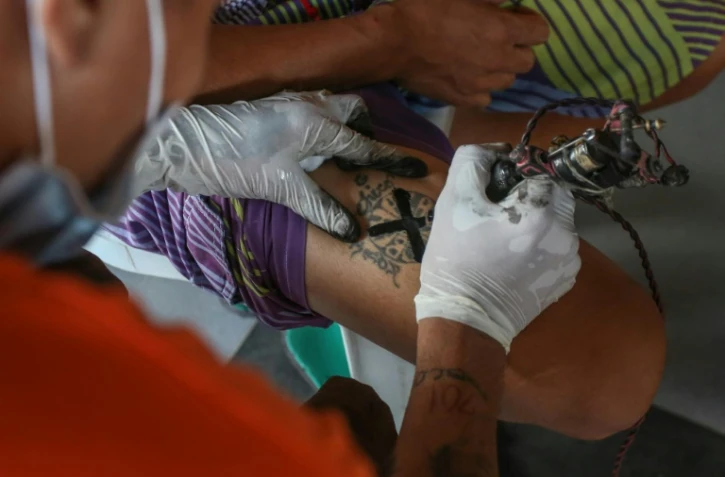 Un tatoueur recouvre d'une croix noire le tatouage qui marque l'appartenance d'un détenu à un gang, le 23 novembre 2020 à la prison de New Bilibid, à Manille, aux Philippines