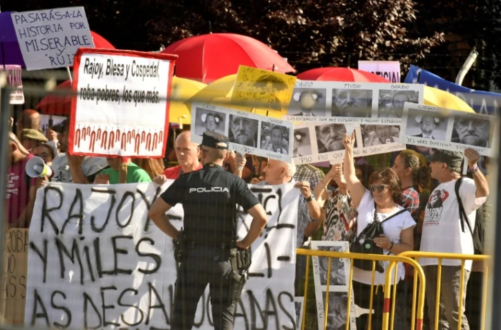 Un policier devant des manifestants qui attendent l'arrivée du chef du gouvernement Mariano Rajoy, entendu comme témoin dans un procès pour corruption, le 26 juillet 2017 à San Fernando de Henares, près de Madrid