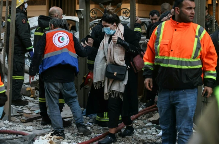 Une femme se fraie un chemin dans  les décombres d'un immeuble où des secouristes interviennent après une frappe aérienne israélienne dans le quartier d'Aïcha Bakkar à Beyrouth, le 11 mars 2026 au Liban