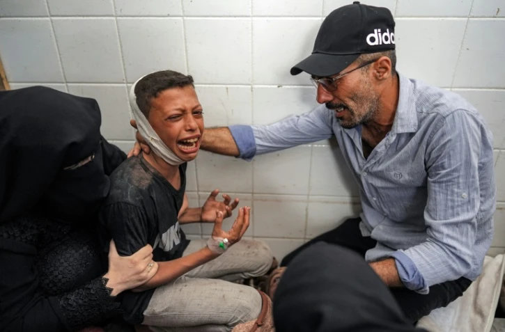 Un homme et une femme réconfortent à la morgue d'un hôpital de Deir el-Balah dans le centre de Gaza, un garçon blessé qui pleure la perte de son père tué dans un bombardement israélien, le 25 juin 2024