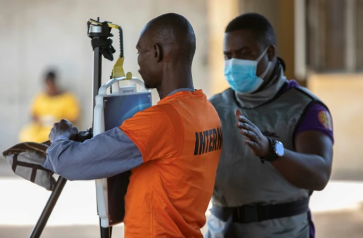 Un membre du personnel médical guide un détenu devant un appareil à rayons X relié à un programme d'intelligence artificielle, à la prison de Maputo, le 6 novembre 2023 au Mozambique