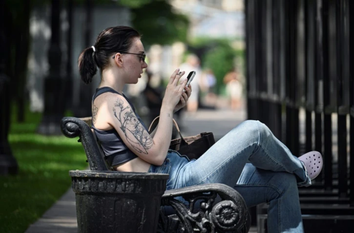 Une femme assise sur un banc utilise son smartphone à Moscou, le 30 juillet 2025