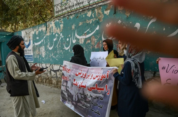 Un membre des talibans parle à des manifestantes devant une école à Kaboul le 30 septembre 2021 tandis qu'un autre tente de cacher l'objectif de l'appareil photo 