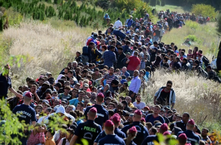 Des migrants encadrés par la police hongroise traversent la campagne le 21 septembre 2015 après avoir franchi la frontière entre la Croatie et la Hongrie près de Zakany