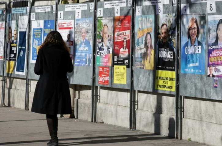 Une femme passe devant un panneau électoral avec les candidats à la mairie de Paris, le 9 mars 2026, à Paris