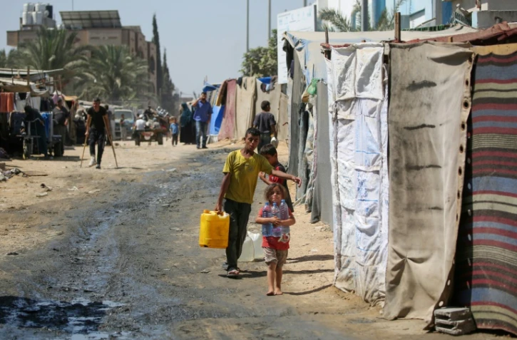 Des enfants déplacés transportent de l'eau jusqu'à leur tente dans un camp de fortune à Deir al-Balah, dans le centre de la bande de Gaza, le 26 août 2024, sur fond de guerre entre Israël et le mouvement palestinien Hamas