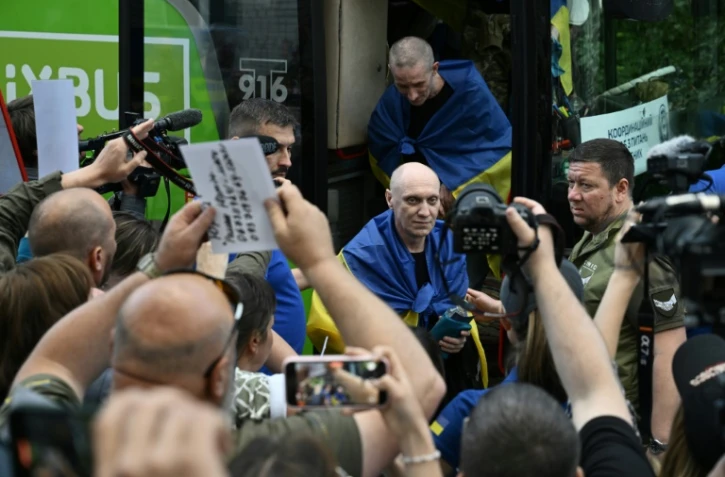 Des prisonniers de guerre ukrainiens libérés enveloppés dans le drapeau national débarquent d'un bus à leur arrivée après un échange de prisonniers dans la région de Tcherniguiv, le 26 juin 2025, en Ukraine