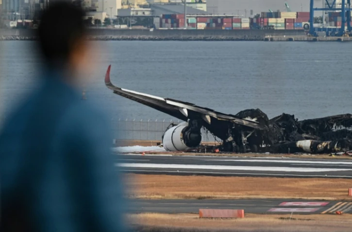 Un homme regarde le 3 janvier 2023 l'avion de ligne de la Japan Airlines qui a pris feu la veille à l'aéroport Tokyo-Haneda après être entré en collision avec un appareil des garde-côtes japonais