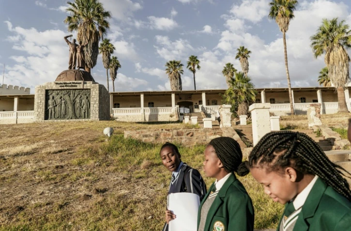 Des jeunes filles en uniforme scolaire passent devant le mémorial aux victimes du génocide commis par les colons allemands en 1904 contre les Hereros et le Namas en Namibie à Windhoek, le 20 juin 2017