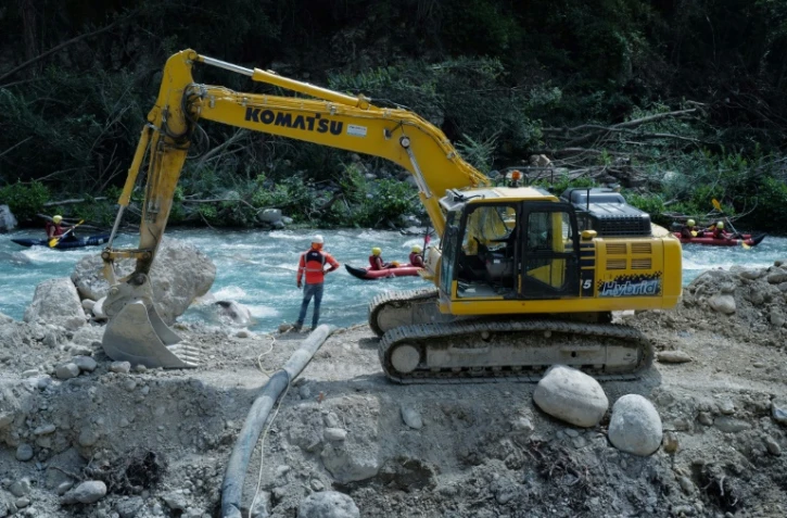 Des touristes en rafting sur la rivière Roya passent près d'un bulldozer reconstruisant une route, dix mois après la tempête Alex, le 12 août 2021 à Breil-sur-Roya, dans les Alpes-Martimes
