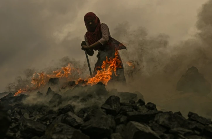 Une jeune femme récupère du charbon au milieu des flammes dans une mine de charbon à ciel ouvert, à la périphérie de Dhanbad, le 6 juillet 2023 en Inde