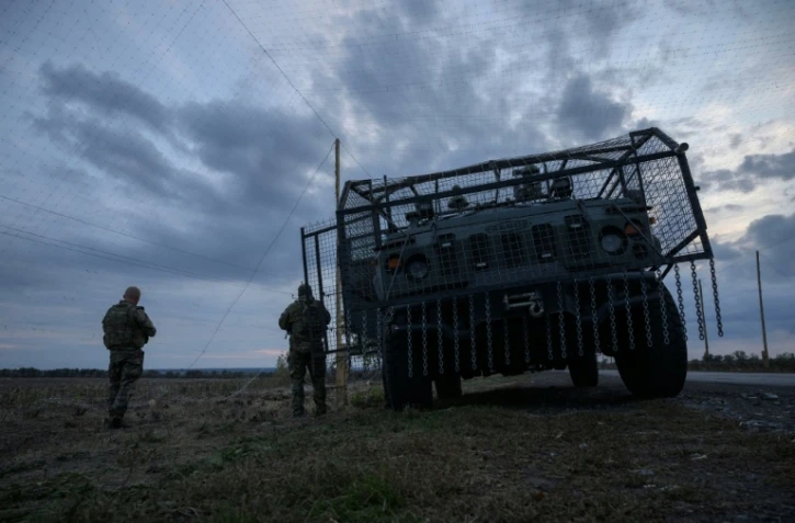 Des soldats ukrainiens devant un véhicule militaire blindé entouré d'une cage de protection contre les attaques de drones, sur une route près d'Oleksandrivka, le 6 octobre 2025