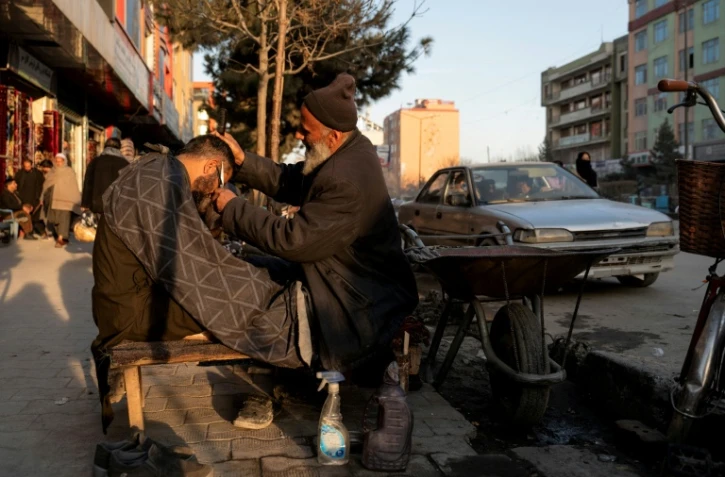 Un barbier coupe les cheveux d'un client dans une rue de Kaboul le 11 février 2026