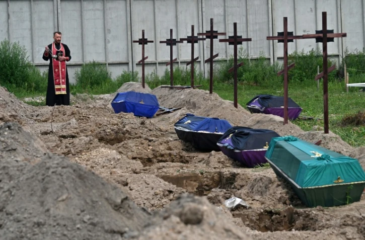 Le prêtre orthodoxe Andriy Golovin récite une prière sur les tombes de civils non identifiés, lors de leurs funérailles dans un cimetière de la ville de Boutcha, dans la région de Kyiv, le 11 août 2022