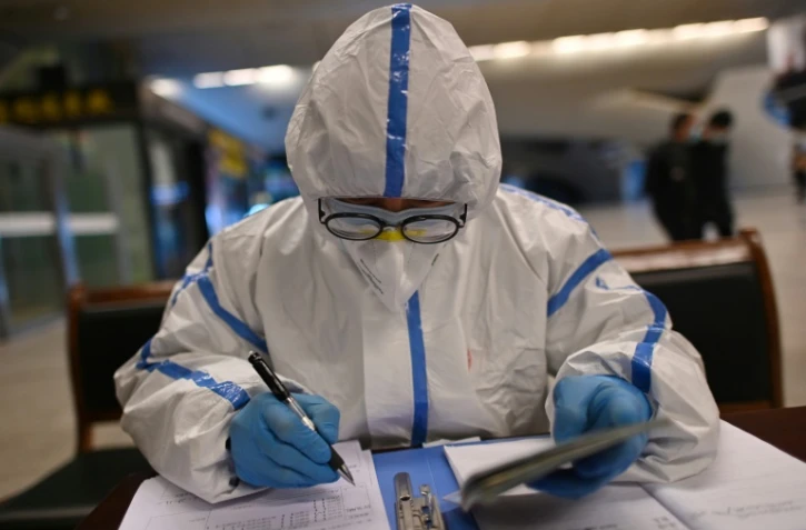 Un employé en combinaison de protection vérifie les documents d'identité des voyageurs arrivant à la gare de Wuhan, dans la province chinoise du Hubei, le 28 mars 2020