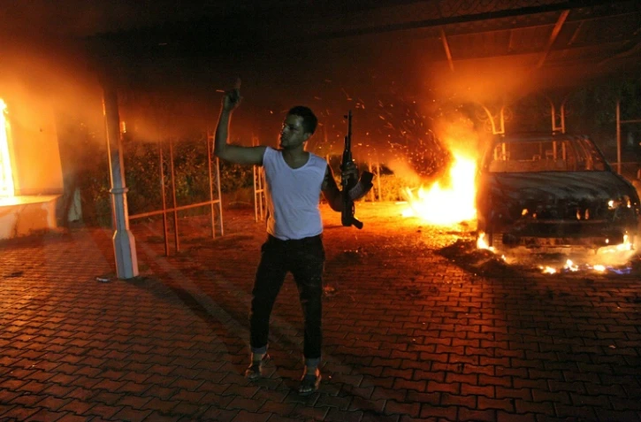 Un homme armé agite son fusil alors que des bâtiments et des voitures sont en flammes après avoir été incendiés à l'intérieur de l'enceinte du consulat américain à Benghazi, en Libye le 11 septembre 2012